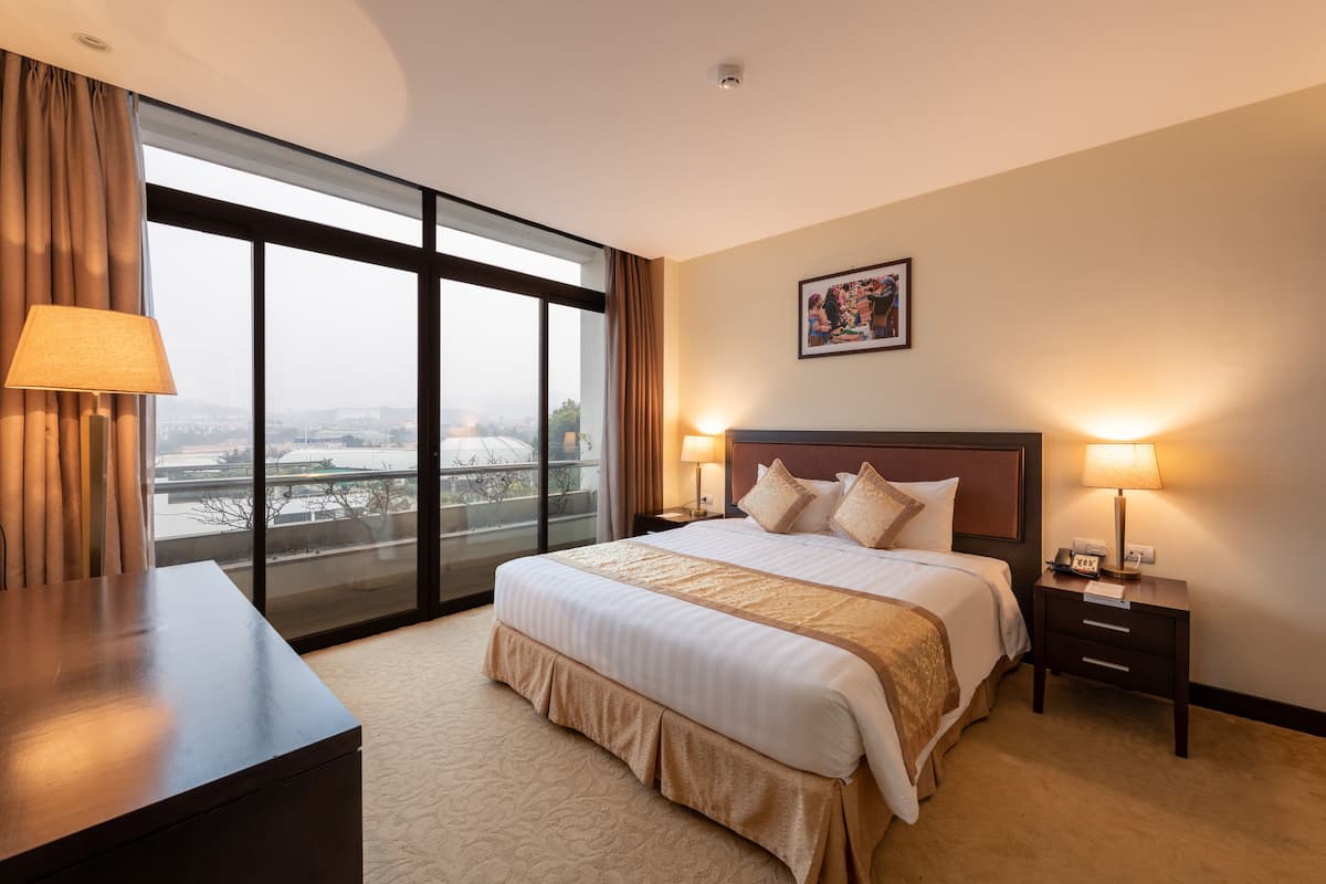 Ein Hotelzimmer mit einem großen Bett, einem Schreibtisch, einem Nachttisch und einem Fenster mit Blick auf die Stadt.