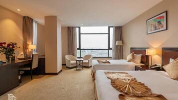 Habitación de hotel con dos camas, un escritorio, una silla, una mesita y una ventana con cortinas.