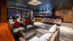 Un espacio lounge moderno con mobiliario de mimbre, una mesa de centro de cristal y una barra con taburetes.