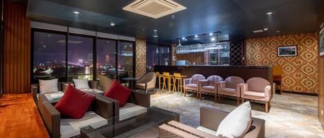 A modern lounge area with wicker furniture, a glass coffee table, and a bar with stools.