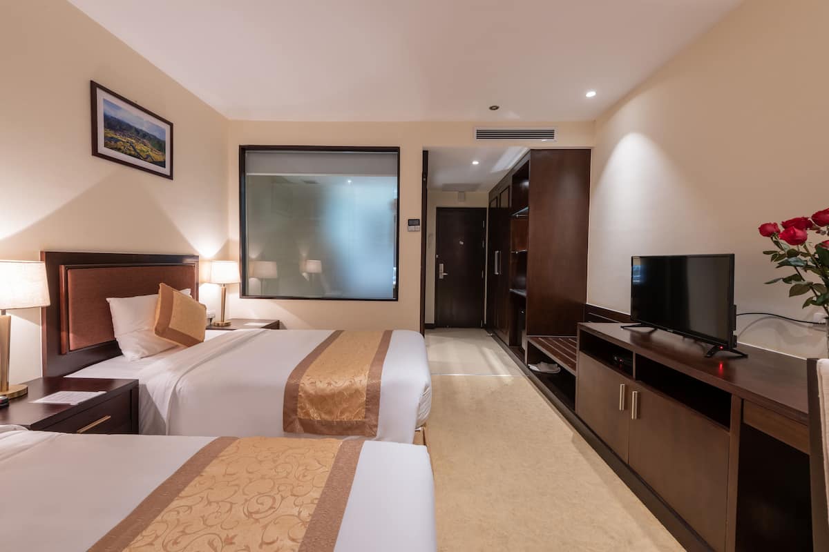 Ein Hotelzimmer mit zwei Betten, einem Fernseher, einem Schreibtisch und einem großen Fenster.