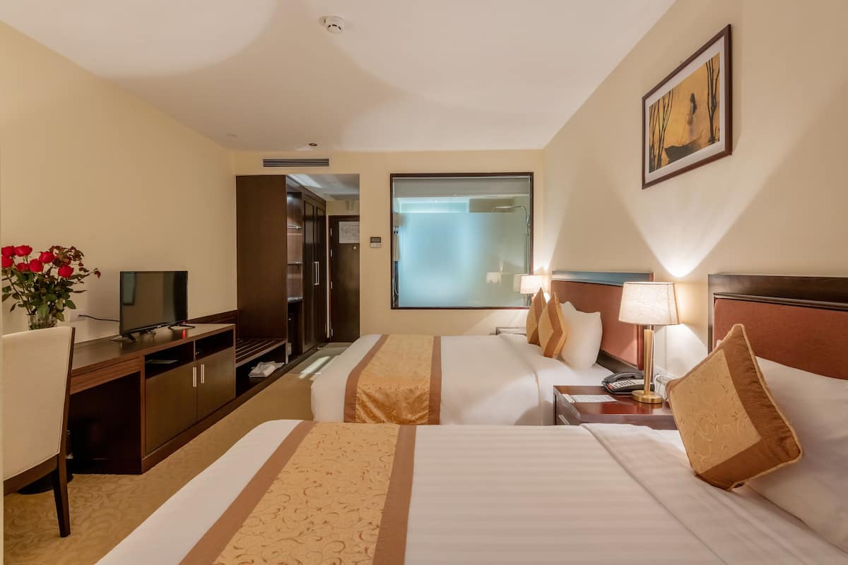 Ein Hotelzimmer mit zwei Betten, einem Schreibtisch, einem Fernseher und einem durch eine Milchglasdoor sichtbaren Badezimmer.
