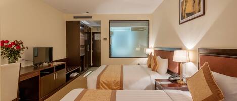 Habitación de hotel con dos camas, un escritorio, un televisor y un baño visible a través de una puerta de vidrio esmerilado.