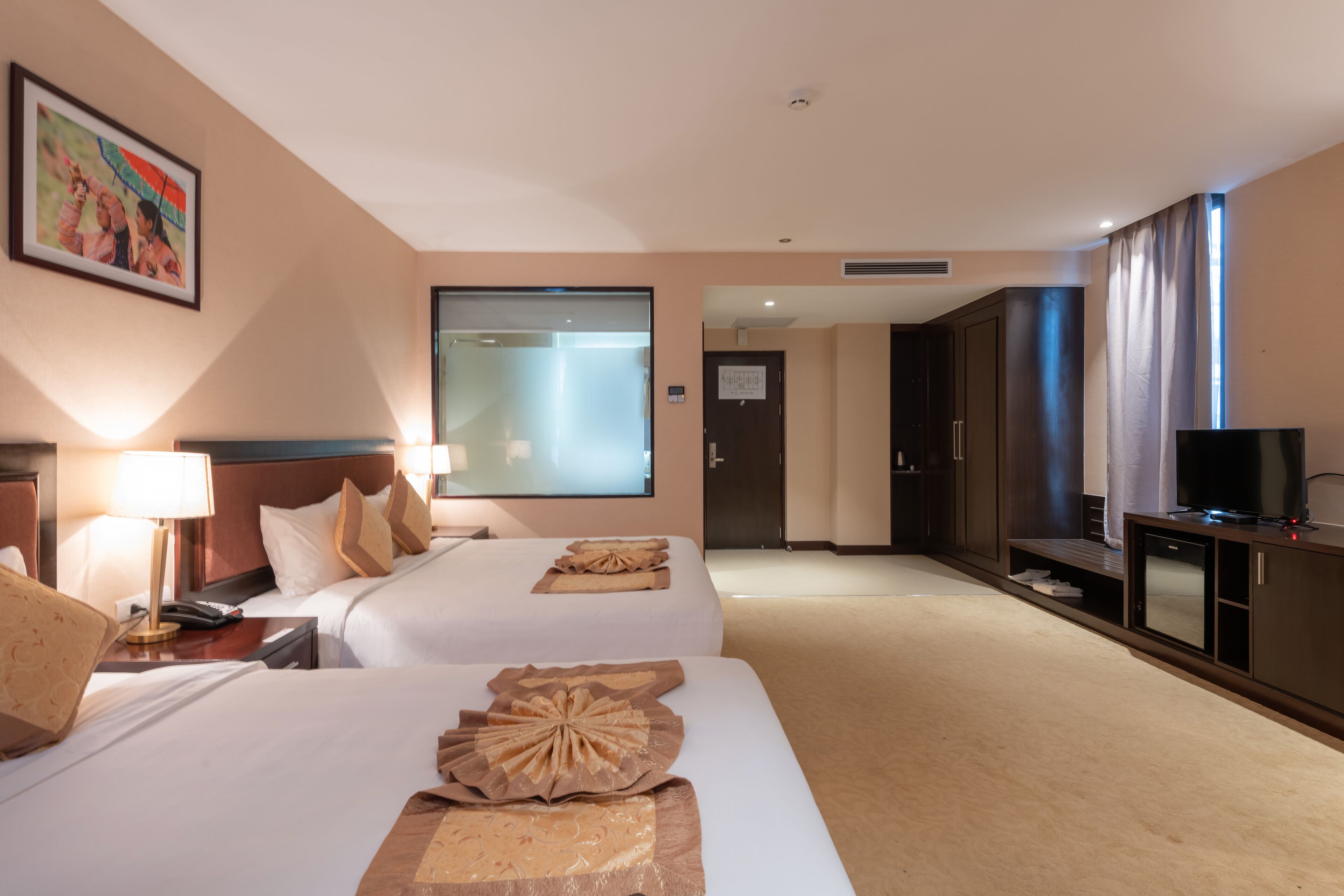 A hotel room with two beds, a TV, a desk with a lamp, and a large mirror.