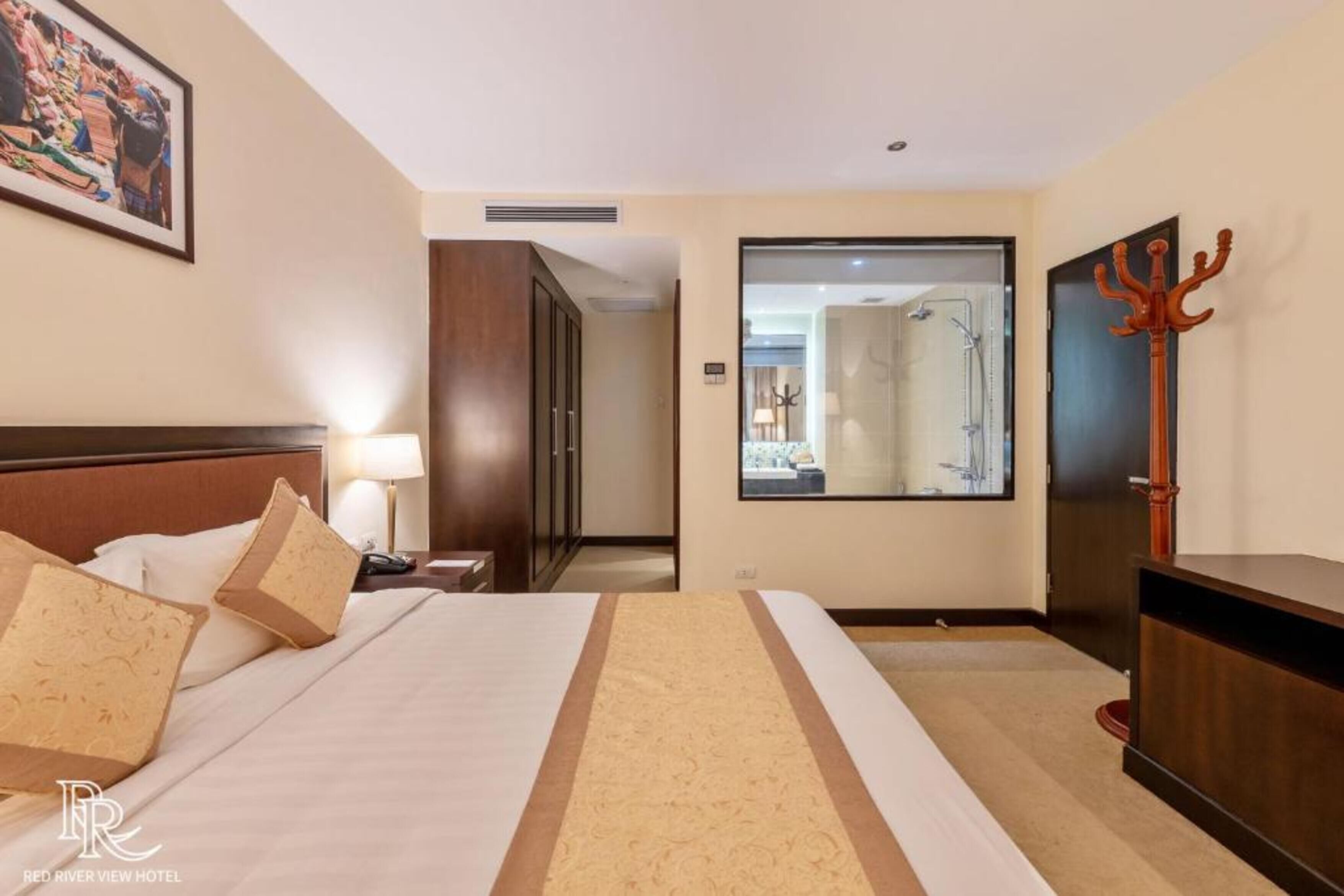 Een hotelkamer met een groot bed, een nachtkastje, een lamp, een houten garderobe en een spiegel.
