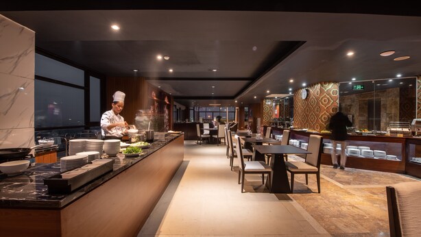 Un restaurante moderno con un chef preparando comida, un área de comedor con mesas y sillas, y una barra con platos.