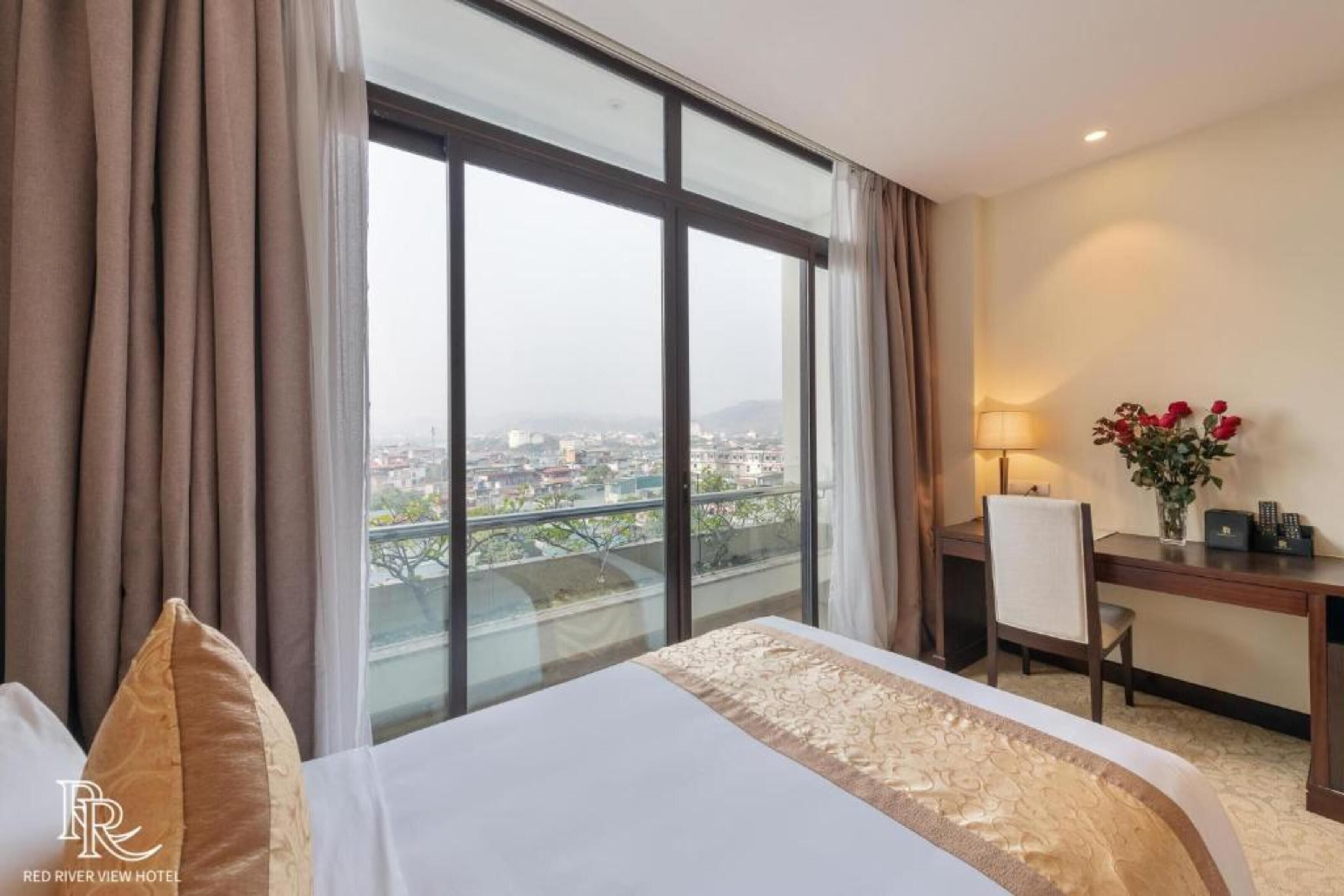 A hotel room with a large window, a bed, a desk, and a chair.