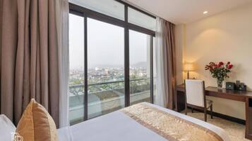 A hotel room with a large window, a bed, a desk, and a chair.