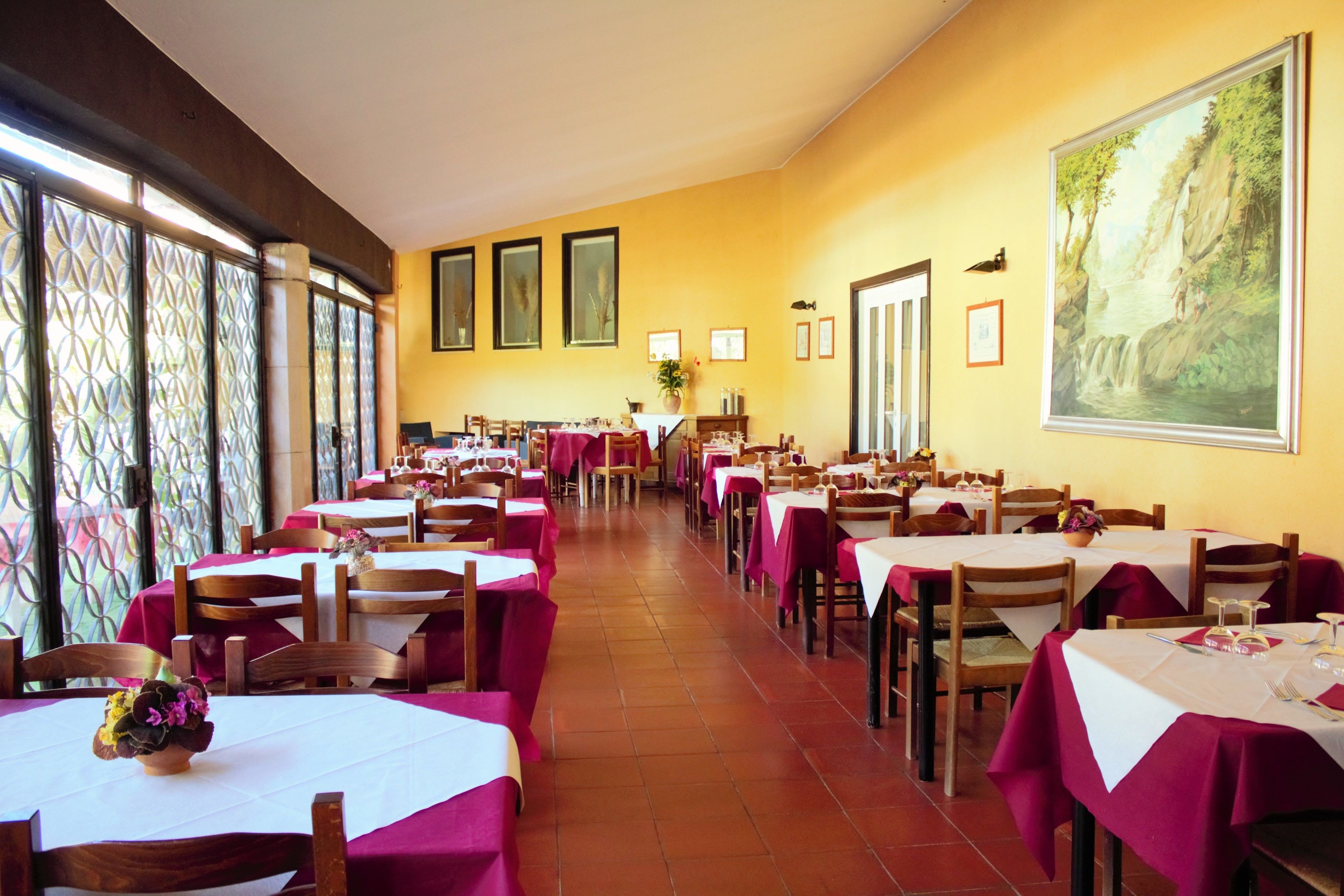 A restaurant with multiple tables and chairs, yellow walls, and framed pictures on the wall.