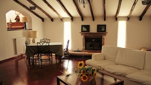 A living room with a fireplace, a sofa, a dining table with chairs, and a coffee table with flowers.