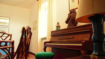 A room with a wooden piano, a green cushioned bench, a tall lamp, and framed pictures on the wall.