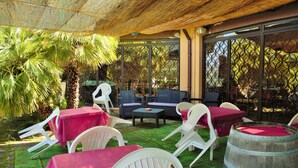 An outdoor patio with white plastic chairs and tables, a wooden barrel, and a palm tree.