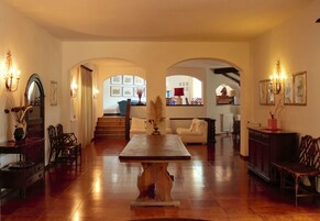 Amplia sala de estar con una mesa de comedor de madera, varias sillas y un sofá. Hay arcos que conducen a otras habitaciones, y el espacio está bien iluminado con luces empotradas.