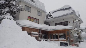 A building with a snow-covered roof and a sign indicating it is a brick house. - Hakuba Cortina Backpackers - Hostel (Otari)