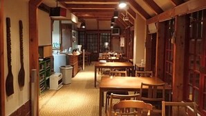 A narrow hallway with wooden beams and tables and chairs arranged on either side. - Hakuba Cortina Backpackers - Hostel (Otari)