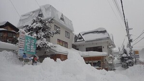 A building with a snow-covered roof and a signboard in front. - Hakuba Cortina Backpackers - Hostel (Otari)