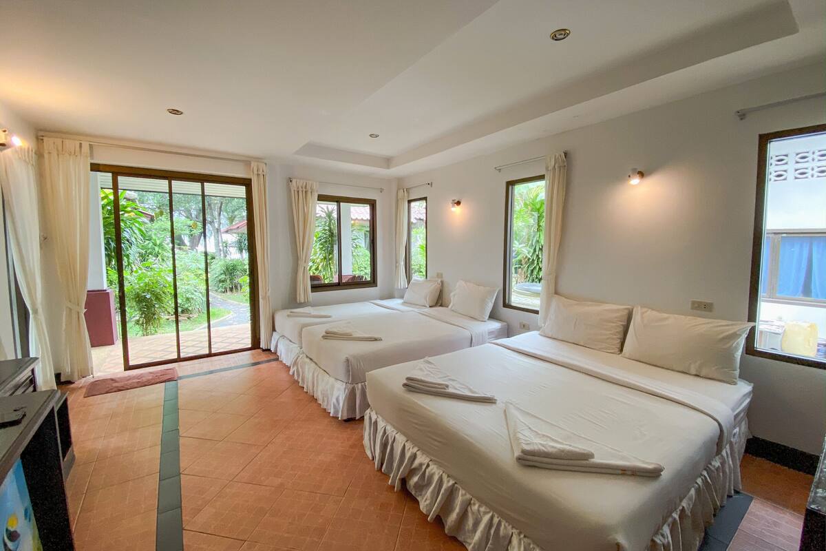 A hotel room with two beds, a sliding glass door leading to a garden, and a small desk with a chair.