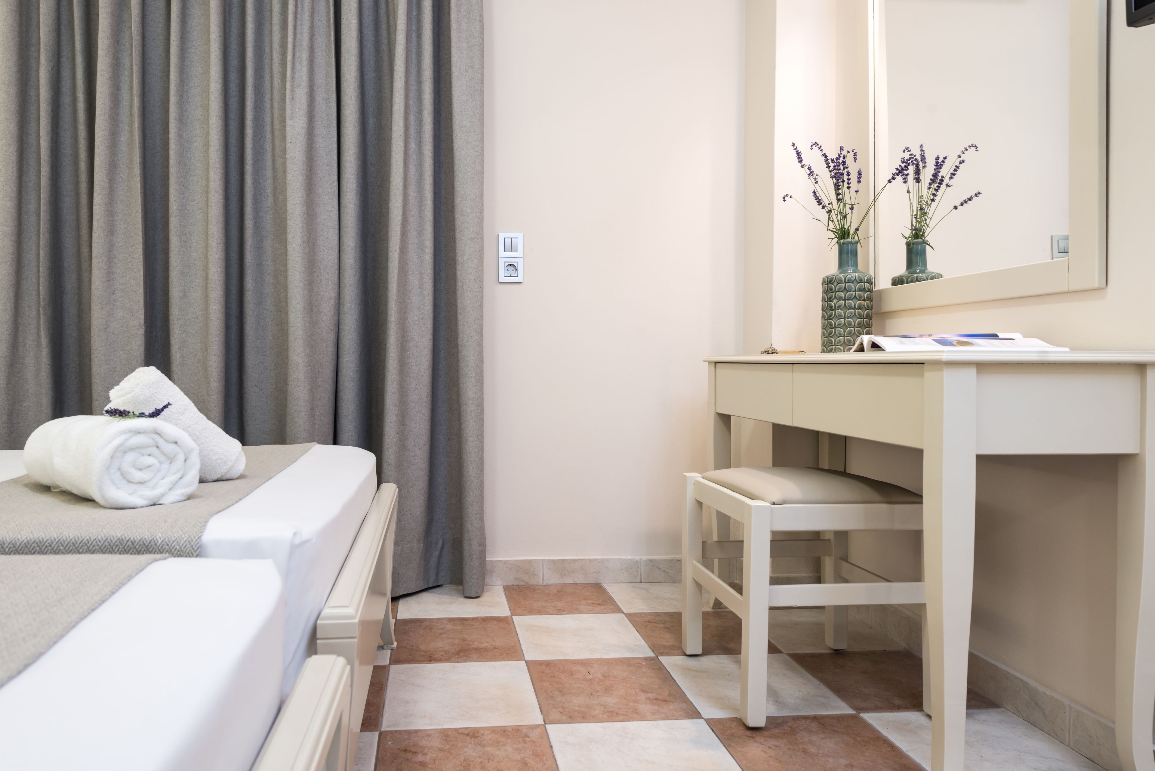 Una habitación de hotel con una cama, una mesita de noche, un espejo y un pequeño taburete.