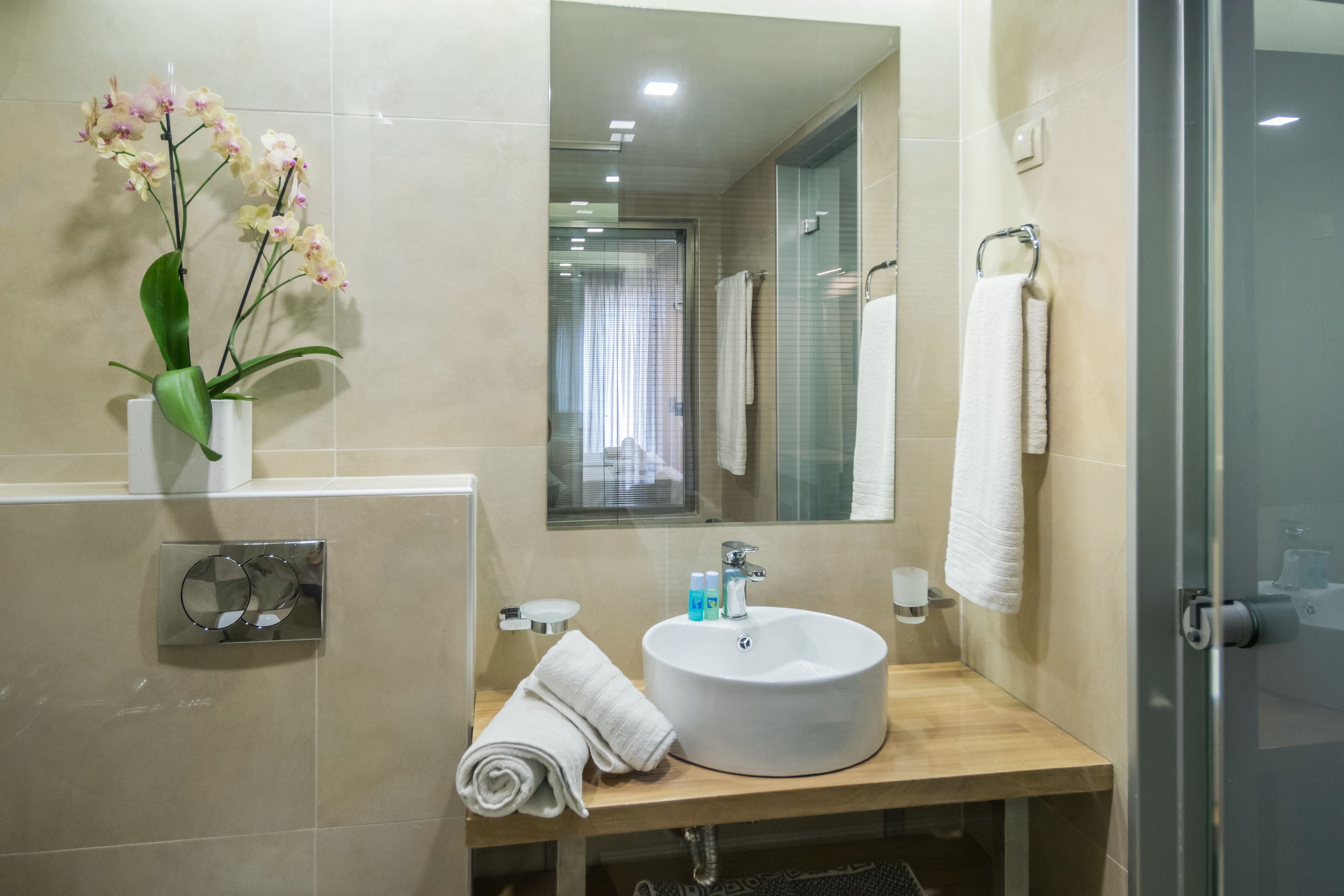 A modern bathroom with a round sink, white towels, a glass shower enclosure, and a vase of orchids.