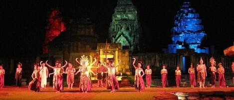 Espectáculo nocturno al aire libre con bailarines vestidos con trajes tradicionales frente a estructuras de templo iluminadas.