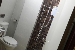 A bathroom with a toilet, a shower with a control panel, and a tiled wall. - R.M. Mansion Surin (Surin)