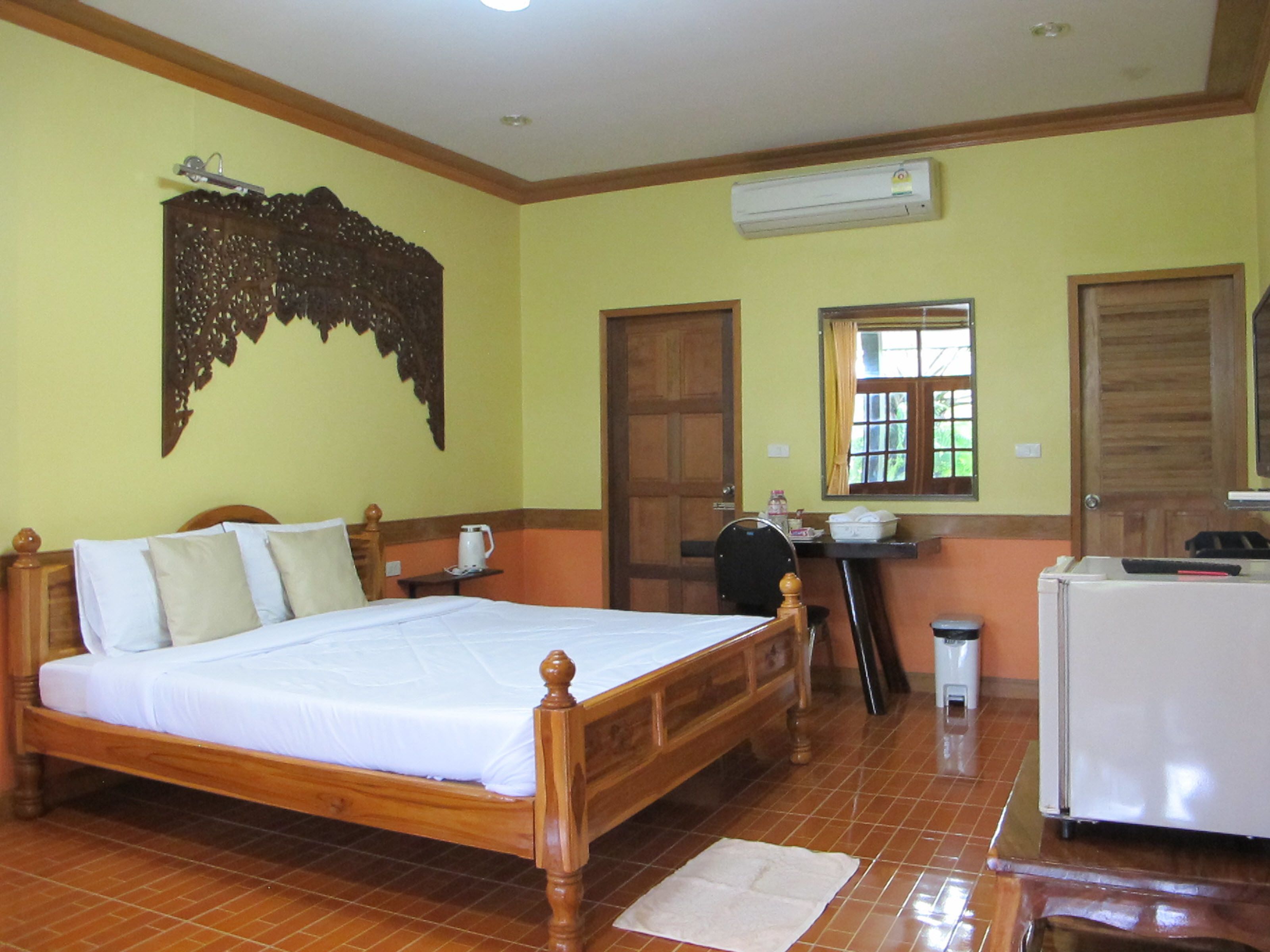 Habitación de hotel con cama de madera, un escritorio con silla, un equipo de aire acondicionado y una ventana con cortinas.