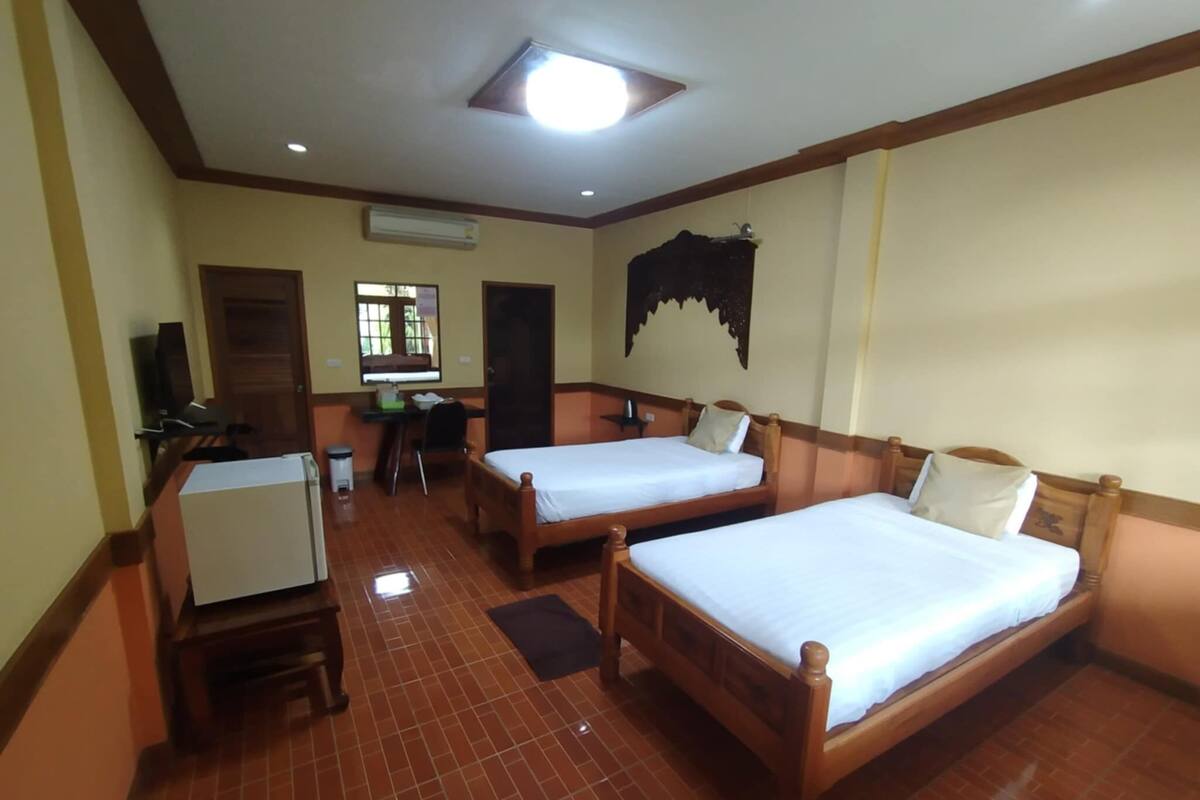 A hotel room with two wooden beds, a desk, a chair, a small refrigerator, and a window with a view.