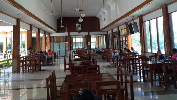 A spacious indoor area with multiple wooden tables and chairs, large windows, and ceiling fans. - Phuendernthang Resort (Tha Chang)
