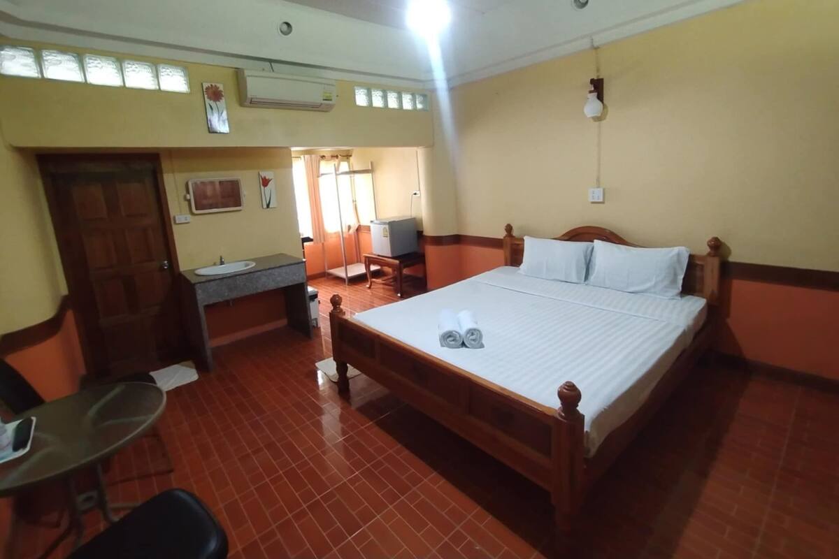 A hotel room with a wooden bed, a desk, a chair, a sink, and an air conditioning unit.