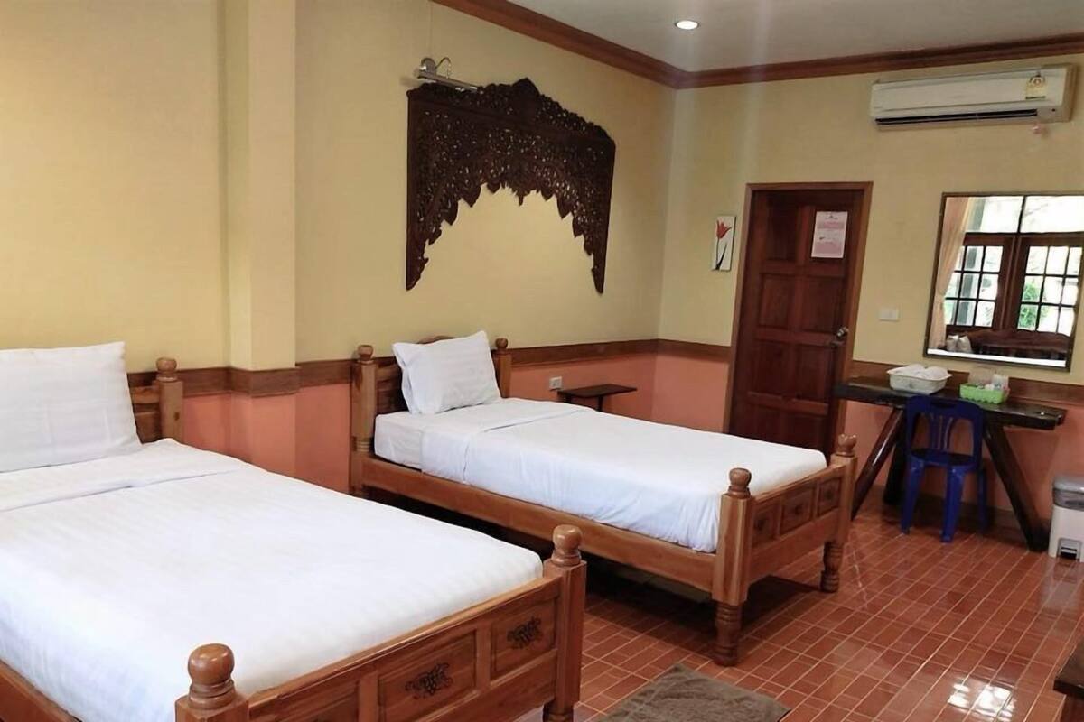 A room with two wooden beds, a desk with a chair, an air conditioning unit, and a window with a view.
