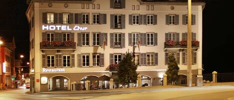 A hotel with a restaurant on the ground floor, multiple balconies, and a well-lit facade at night.