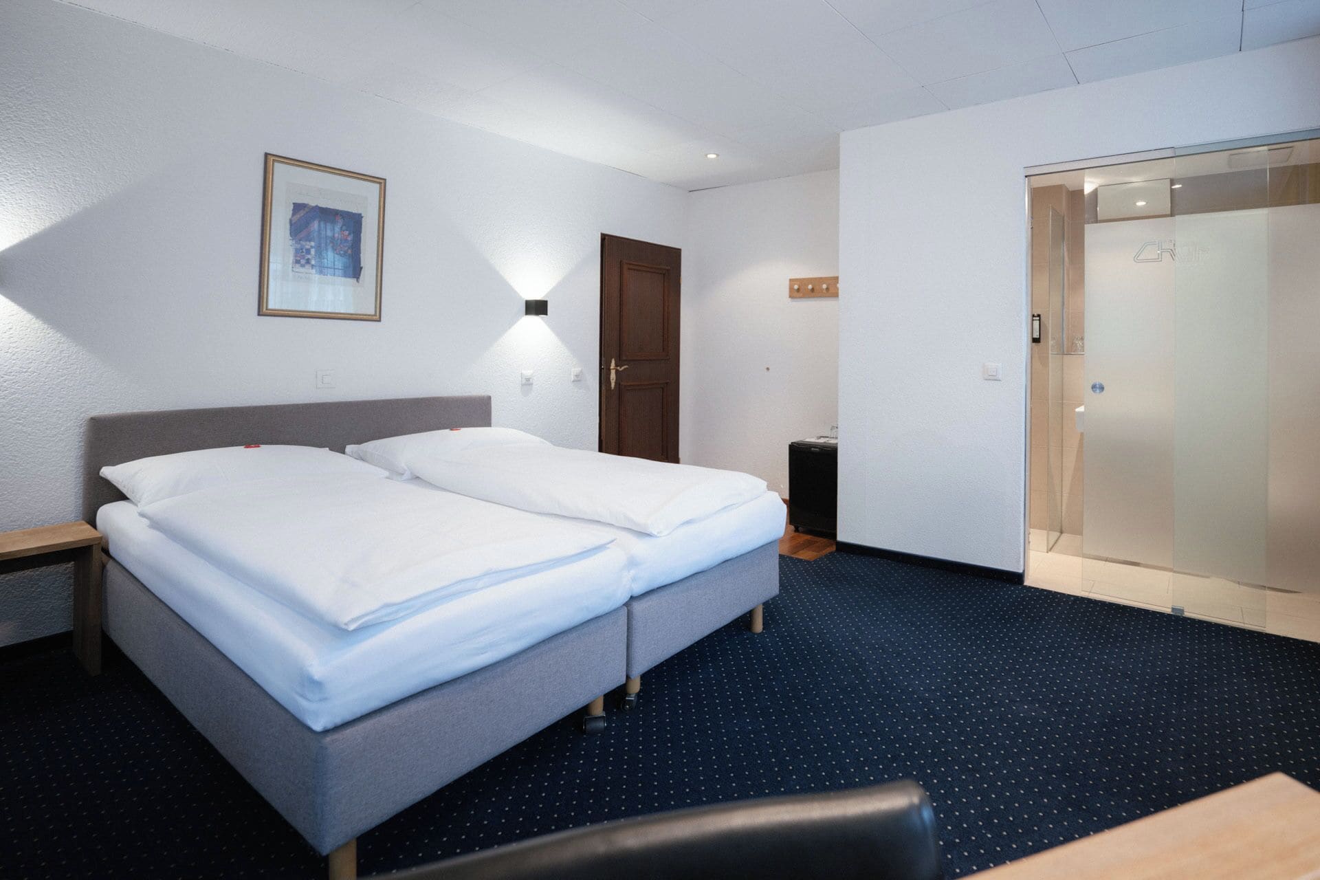 Habitación de hotel con cama doble, escritorio, silla, armario y un cuadro en la pared.