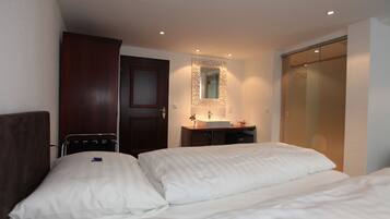 Una camera d'albergo con un letto, un comodino, uno specchio, un armadio e un bagno con lavandino e specchio.