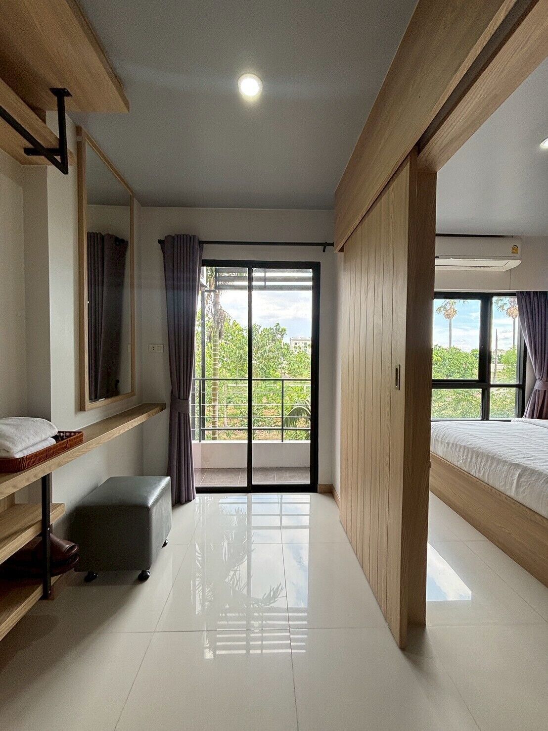 Habitación de hotel con un amplio ventanal corredero, una cama, un tocador con espejo y un pequeño rincón de descanso.