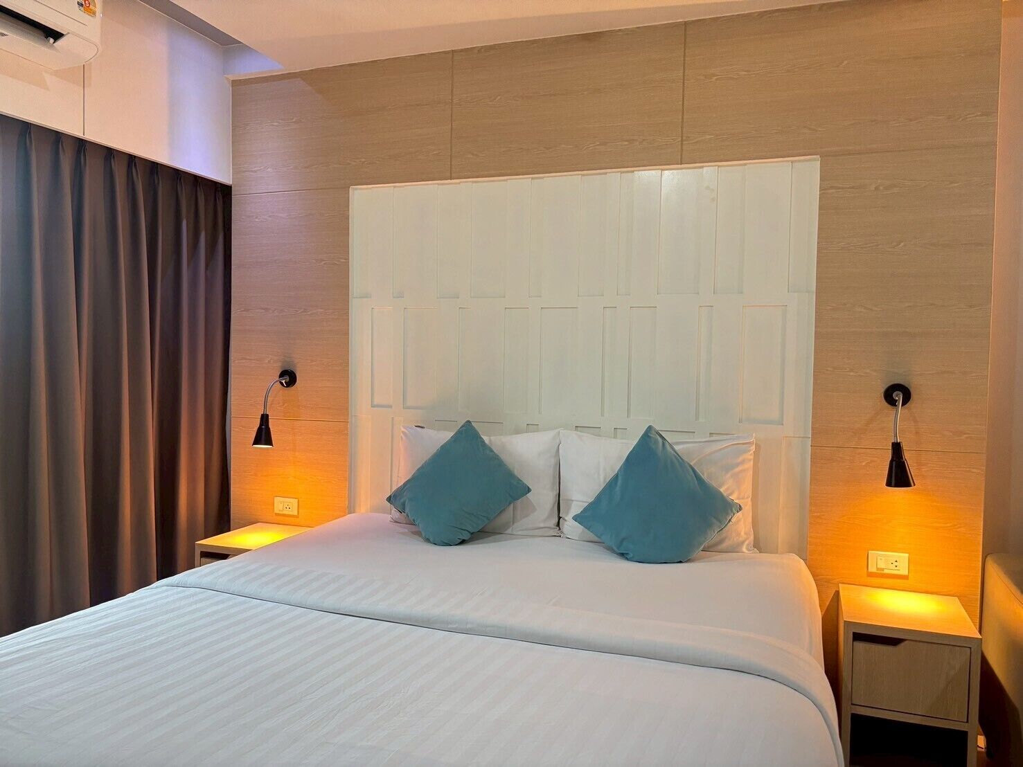 A hotel room with a large bed, two bedside tables with lamps, a headboard, and a curtain.