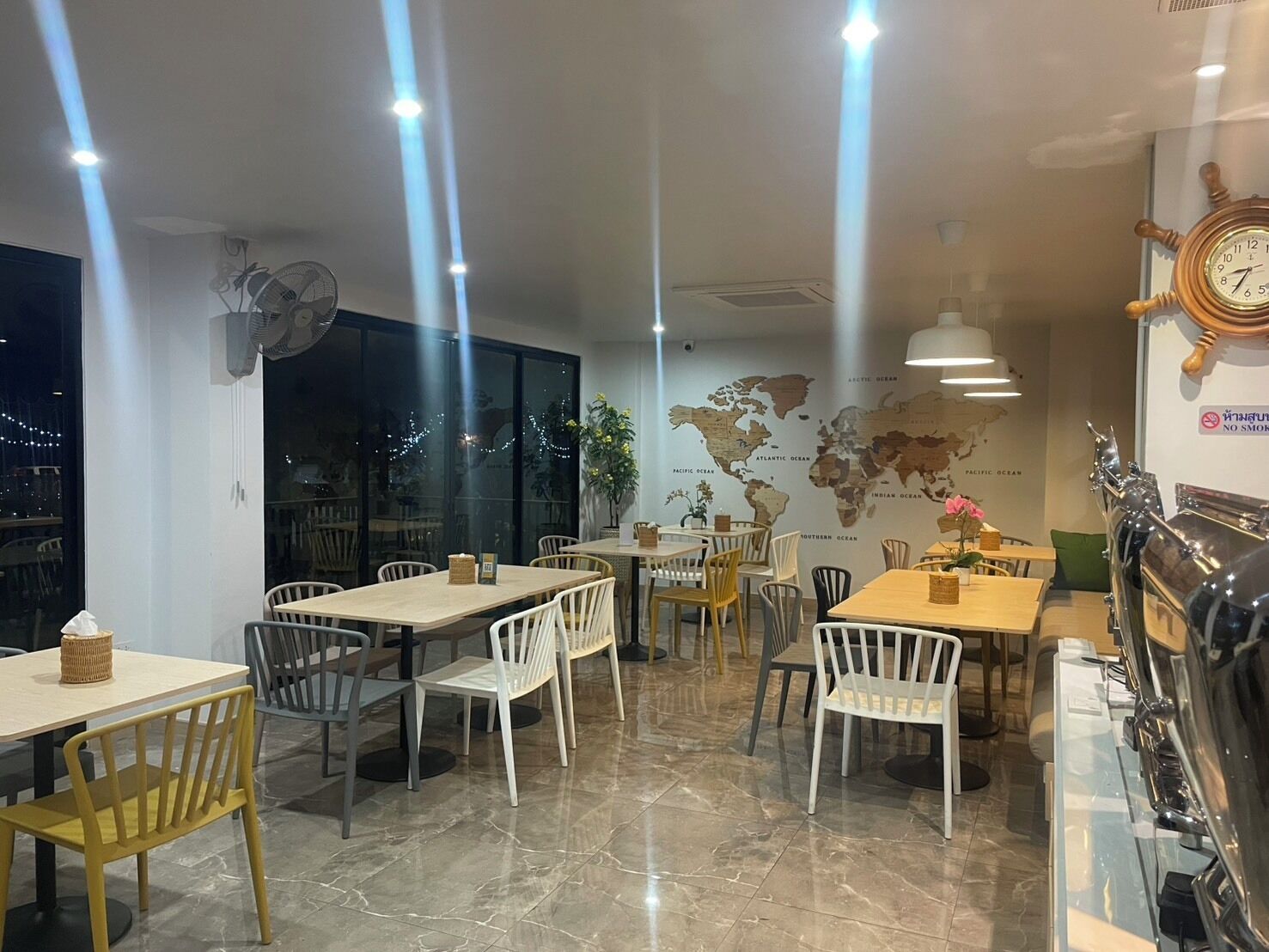A restaurant interior with multiple tables and chairs, a world map on the wall, and a clock.