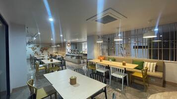 Un comedor moderno con mesas y sillas, una isla central con cafetera y un espacio de estar con sofá y cojines.