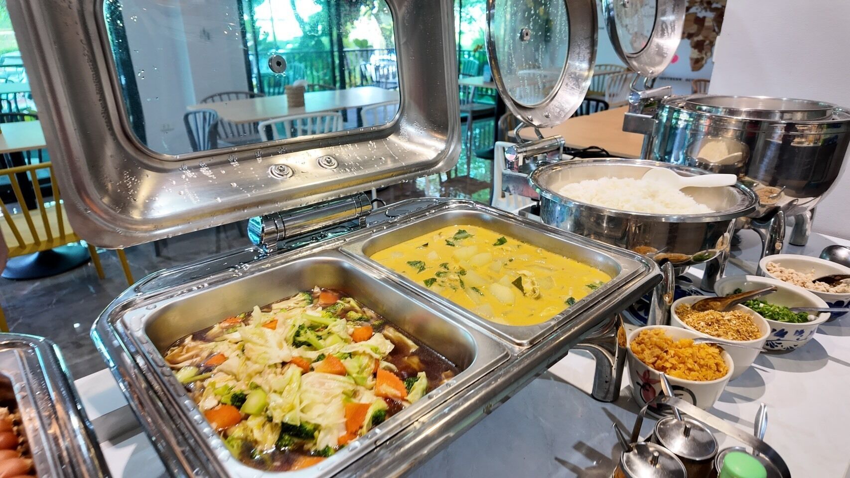 Un bufé con diversos platos, incluyendo un salteado de verduras, un curry amarillo y varios acompañamientos.