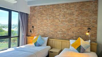 Een hotelkamer met twee bedden, een bakstenen muur, een raam met gordijnen en uitzicht op de stad.