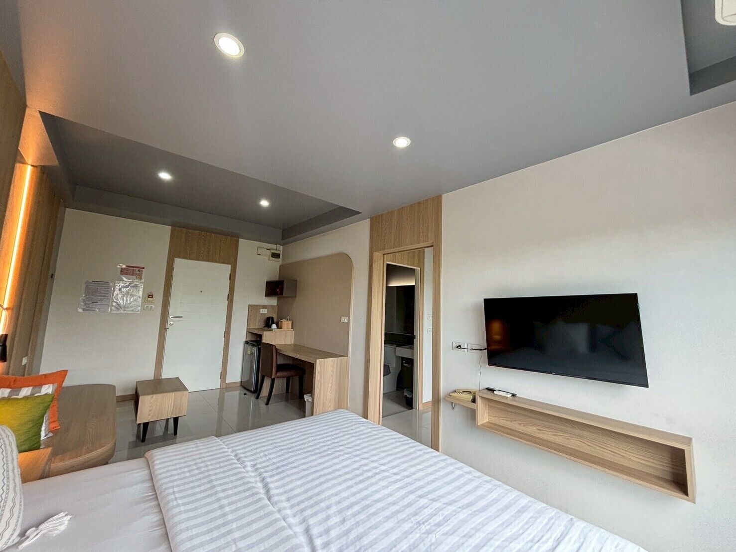 A modern hotel room with a bed, a desk, a chair, a television mounted on the wall, and a small shelf.