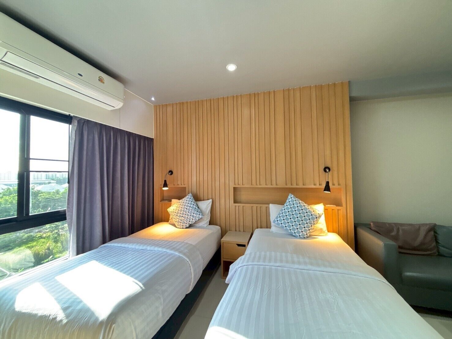 Habitación de hotel con dos camas, un panel de pared de madera, una ventana con cortinas y vistas a zonas verdes.
