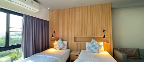 Habitación de hotel con dos camas, un panel de pared de madera, una ventana con cortinas y vistas a zonas verdes.
