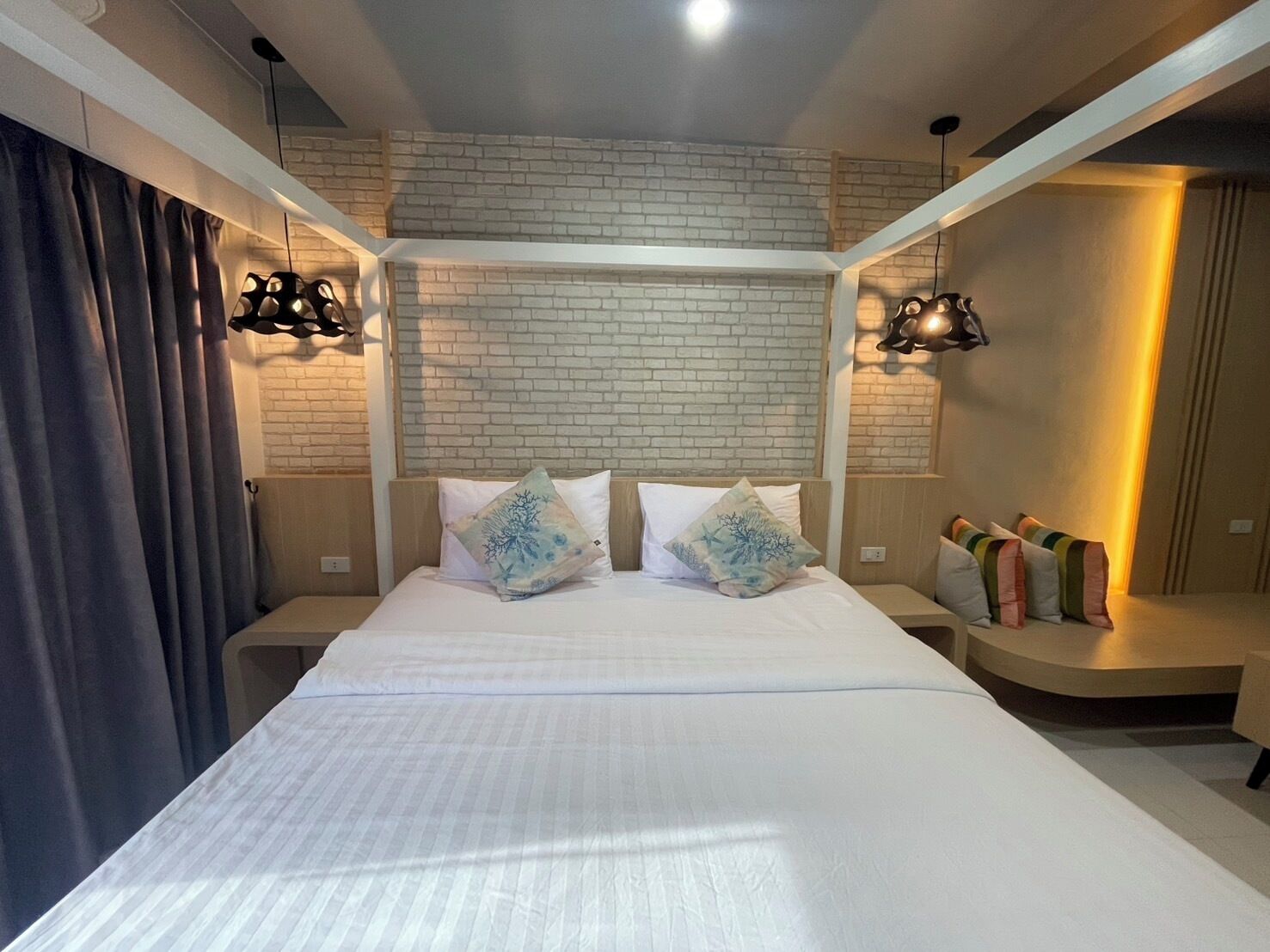 A modern hotel room with a large bed, two nightstands, a brick accent wall, and ambient lighting.