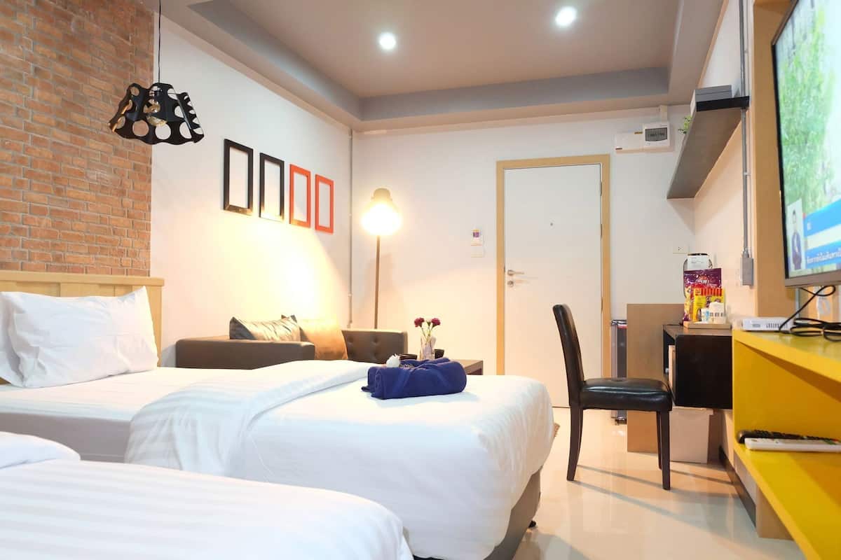 A hotel room with two beds, a desk, a chair, a TV, and a brick wall.