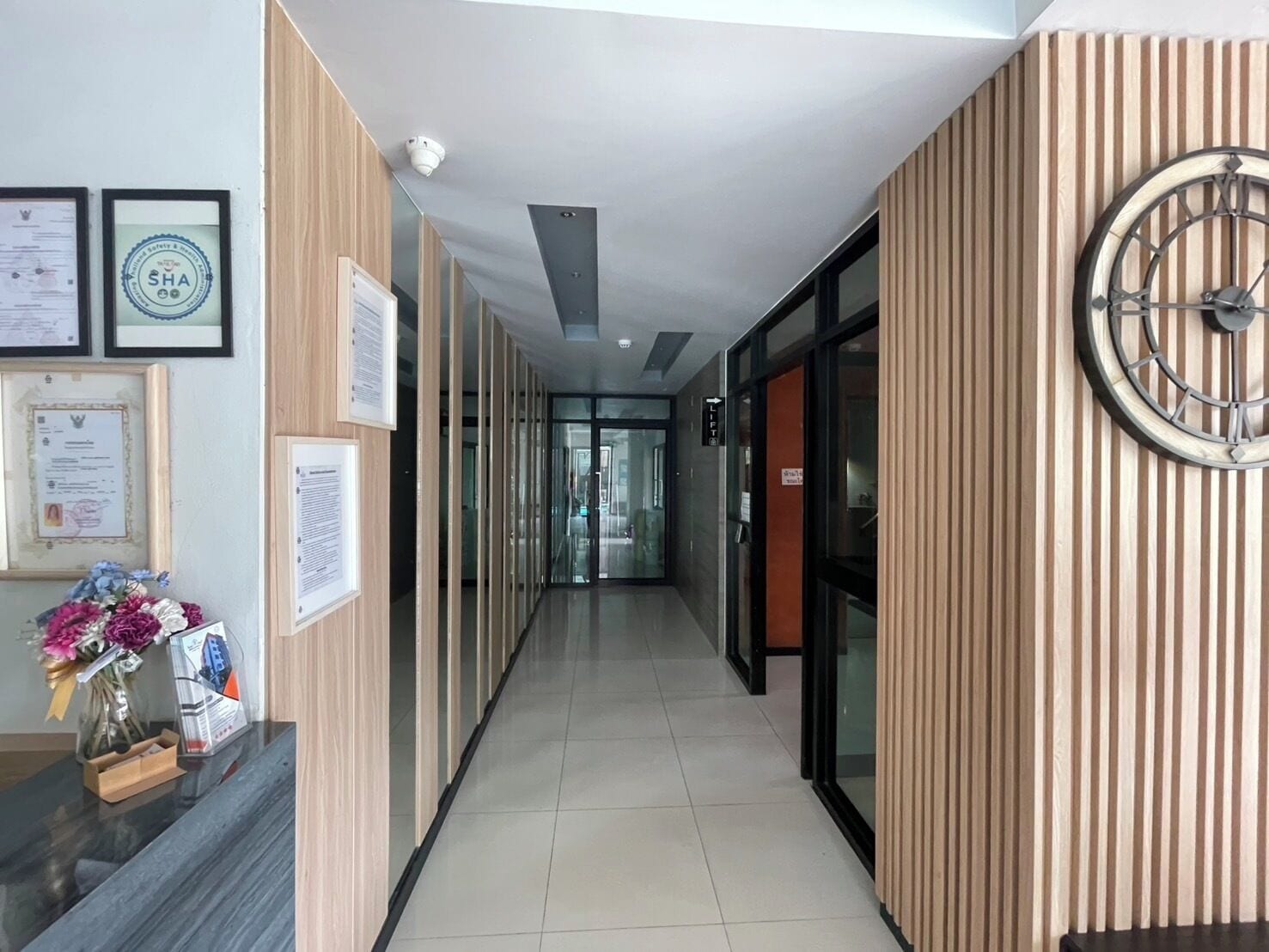 A modern hallway with framed certificates, a clock, and a reception desk with a vase of flowers.