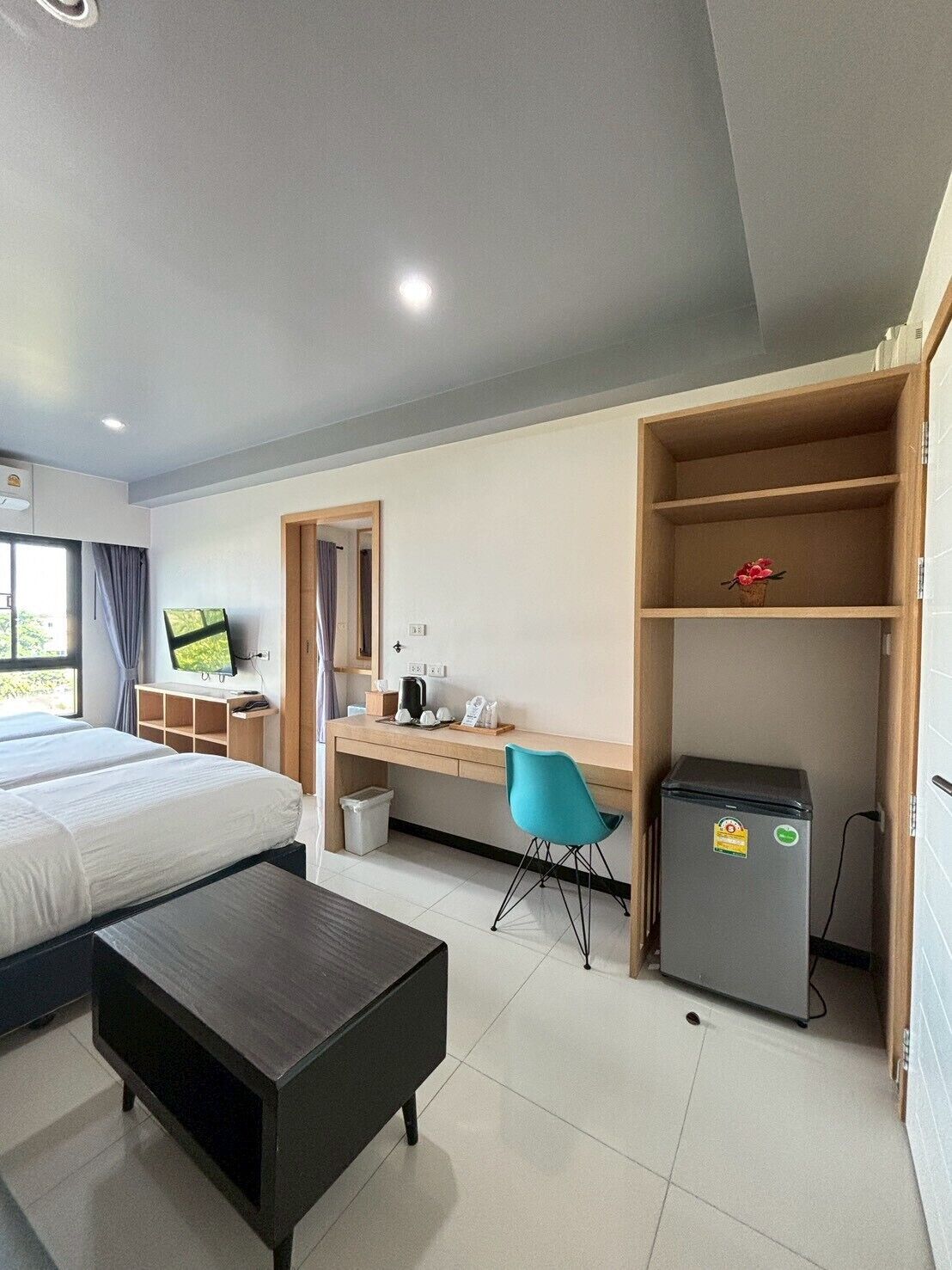 Una habitación de hotel con una cama, un escritorio con silla, un refrigerador pequeño y un televisor en la pared.
