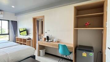 Una habitación de hotel con una cama, un escritorio con silla, un refrigerador pequeño y un televisor en la pared.
