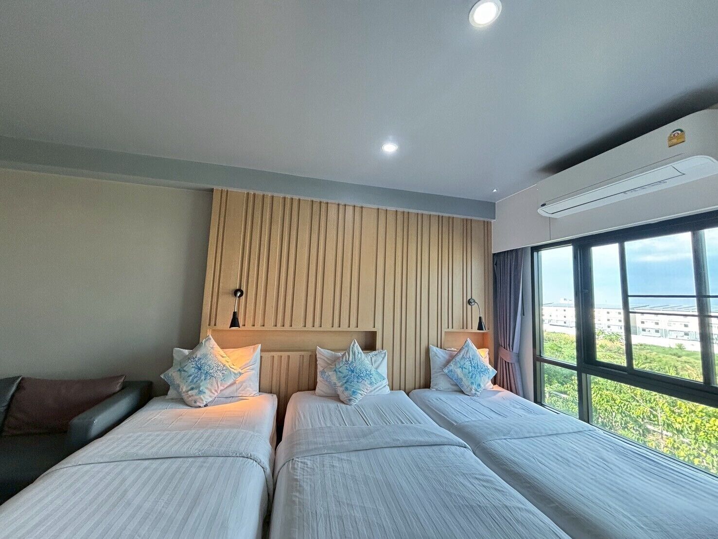 Habitación de hotel con dos camas, un panel de pared de madera, un ventanal con vistas y un equipo de aire acondicionado.