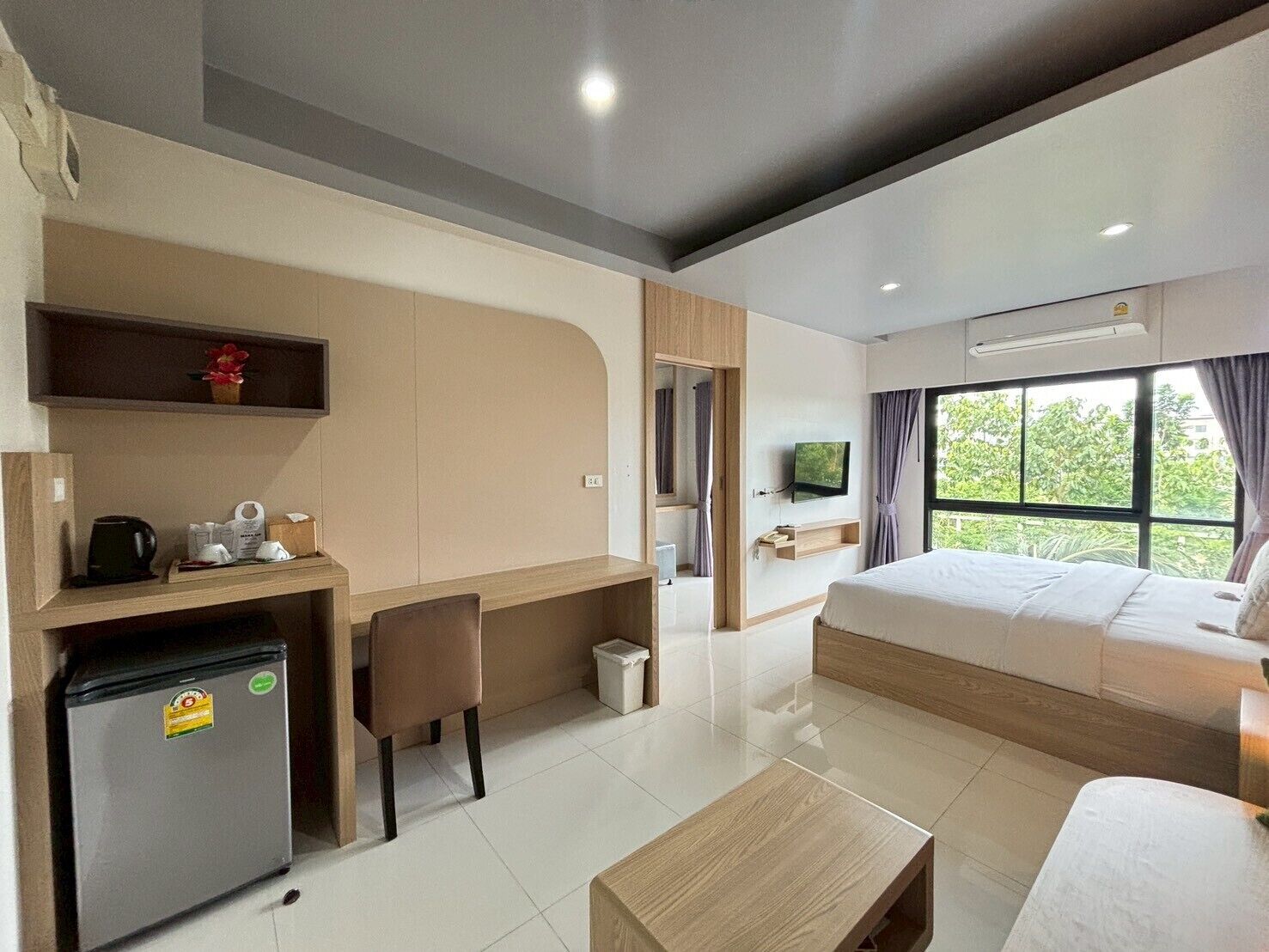 Habitación de hotel con cama, escritorio, silla, cafetera, televisor y ventana con cortinas.