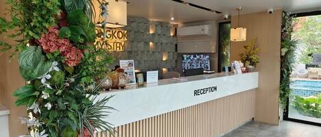 A reception area with a modern design, featuring a reception desk, a stone wall, and a view of a pool.